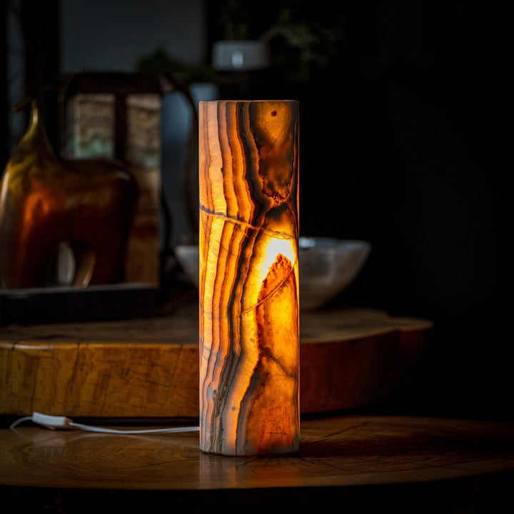 Cylinder table lamp with dark onyx-look shade, emitting warm amber glow