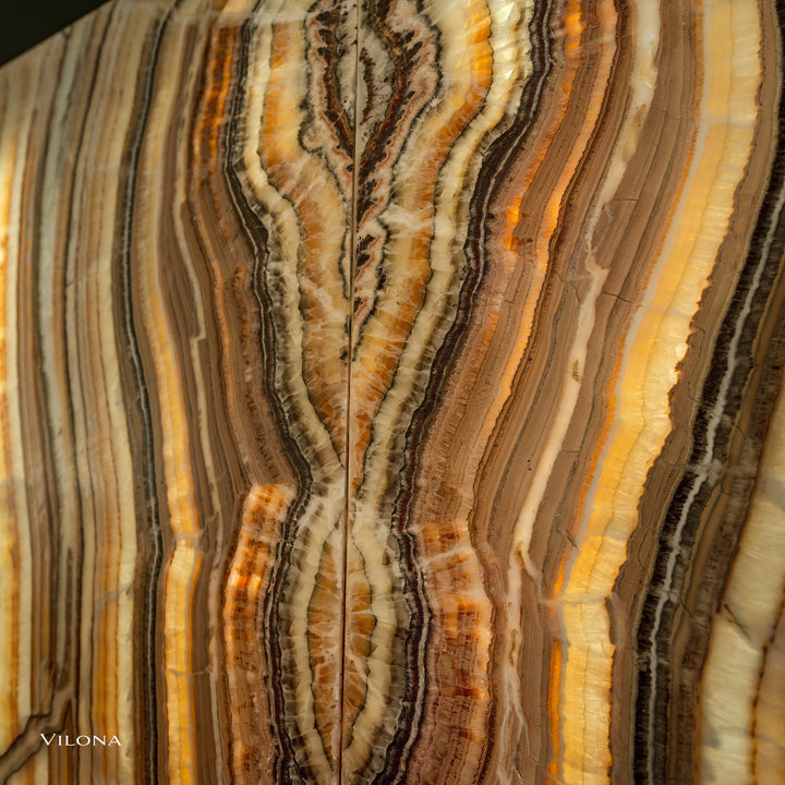 Onyx wall panel close-up with ribbon-like veins in cream, gold, and dark brown