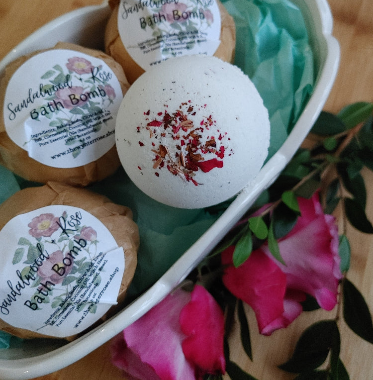 Dusty rose bath bomb with red-pink flower petals, in a tray with other bombs