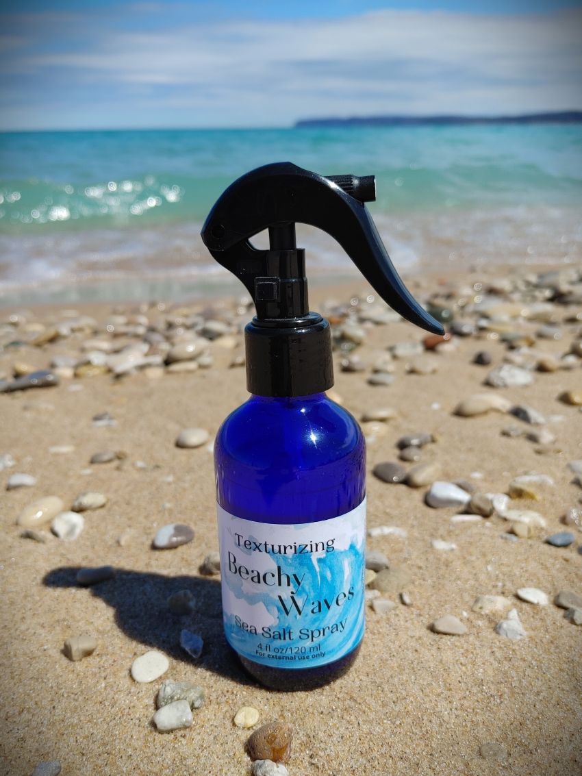 Blue sea salt spray bottle with black trigger sprayer on sandy beach