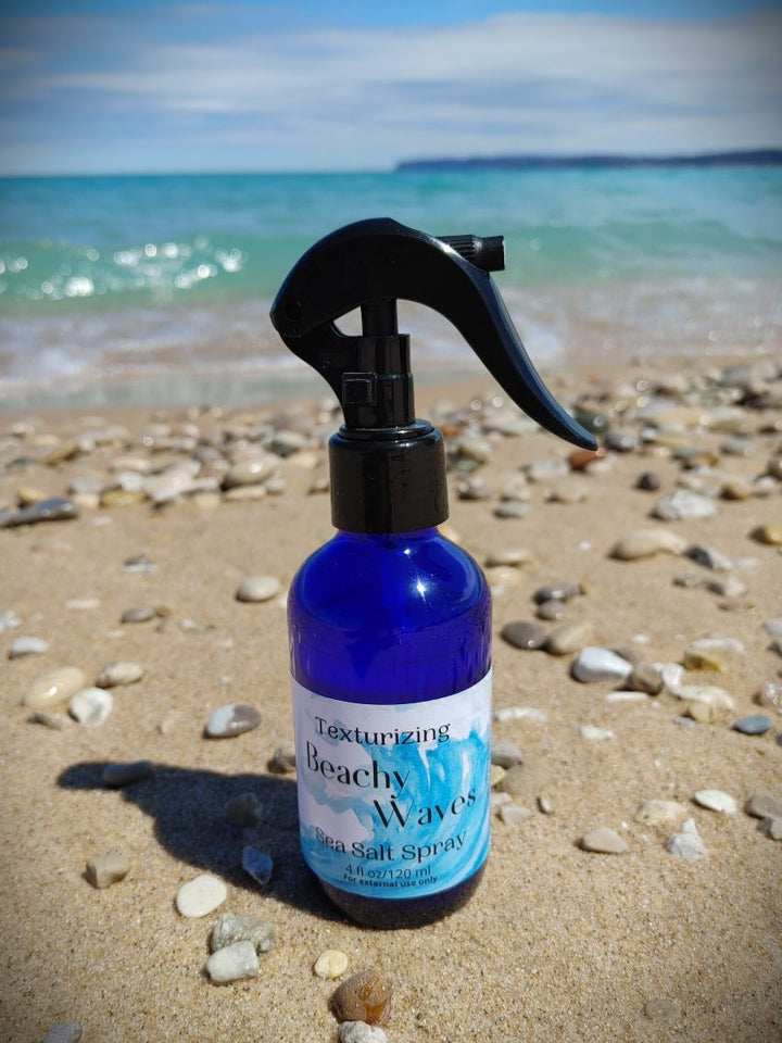 Blue sea salt spray bottle with black trigger sprayer on sandy beach