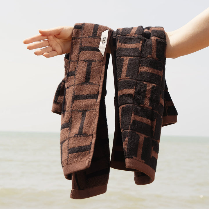 Two folded cotton towels with dark base and brown block grid pattern, held open