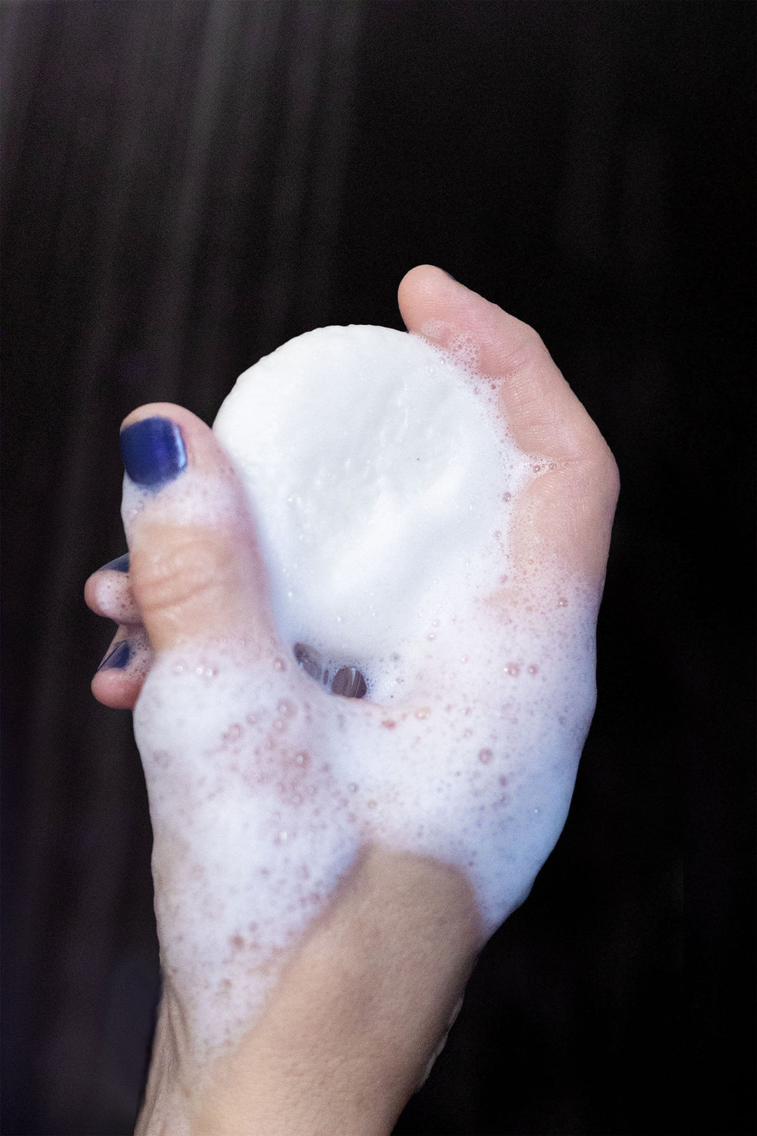 White shampoo bar held in hand with foamy lather