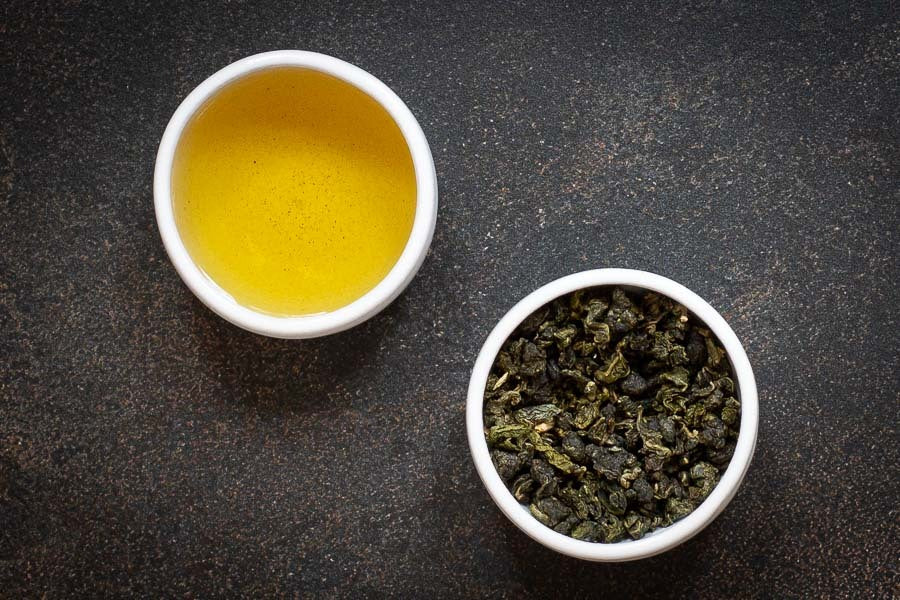 Oolong tea cup with golden infusion and loose green leaves in a small bowl