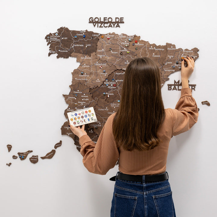 Person placing Spain flag pins on wall-mounted wooden map