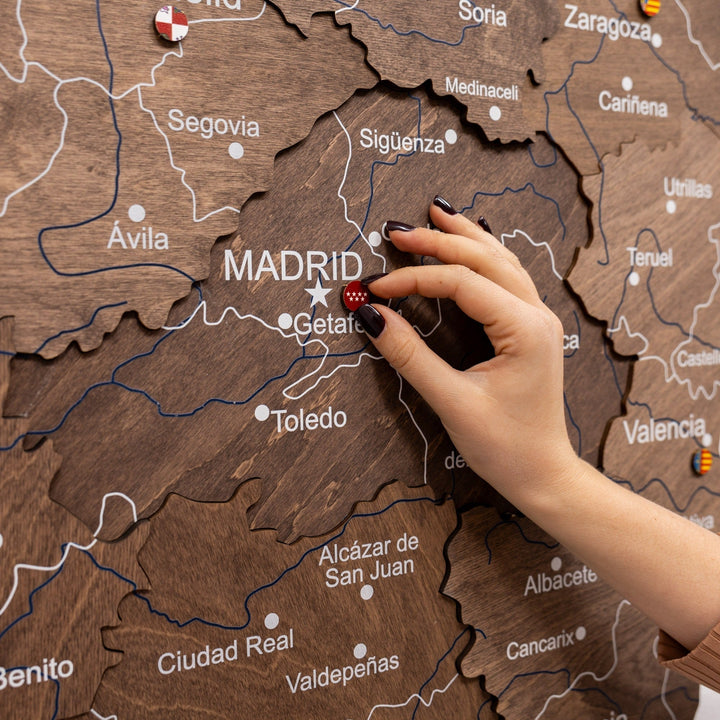 Hand arranging flag pins on wooden Spain map near Madrid