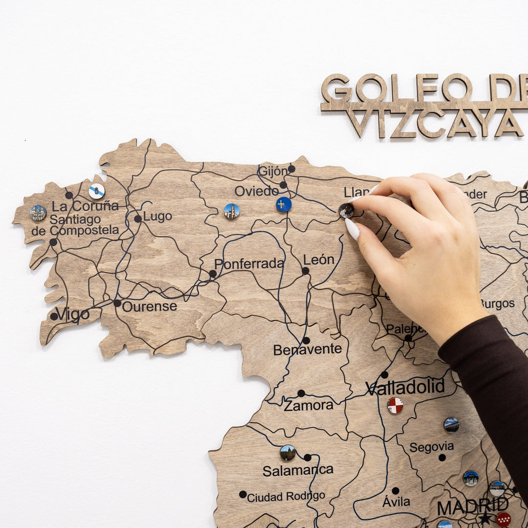 Spain landmark enamel pins on wooden map board, hand attaching round pin near labels