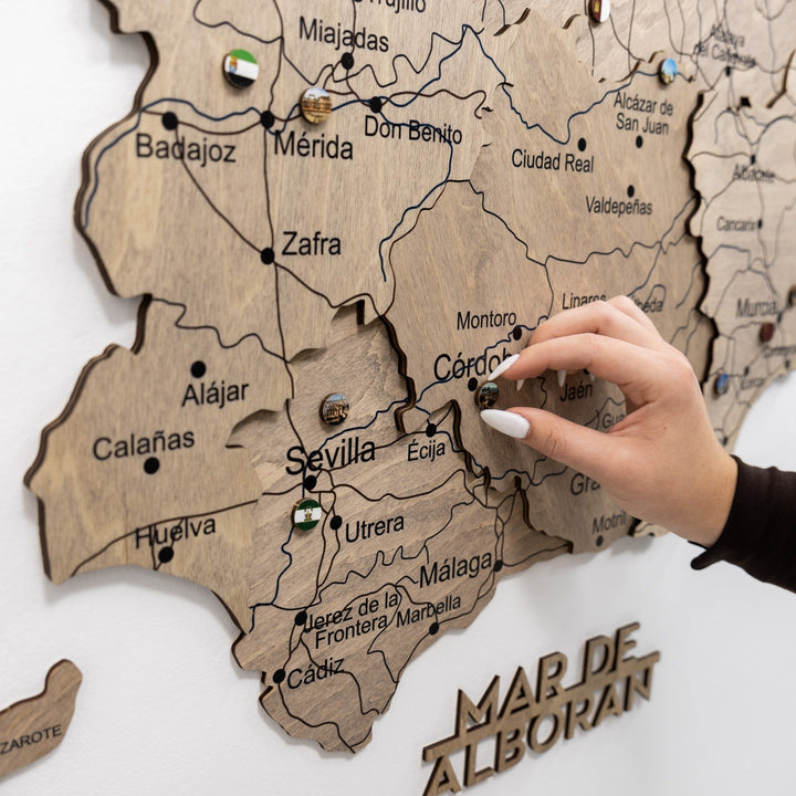 Hands placing round Spain landmark enamel pins onto a wooden map board