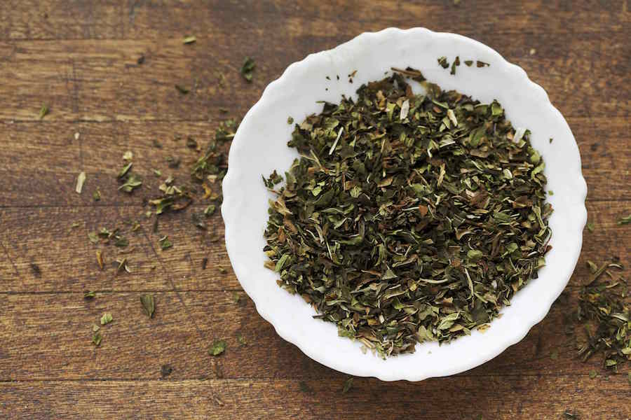 Spearmint loose tea leaves in white ceramic dish on wooden surface