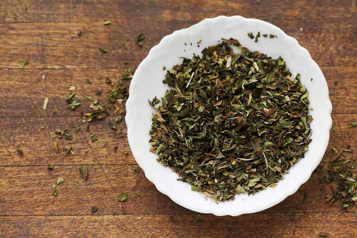 Spearmint loose tea leaves in white ceramic dish on wooden surface