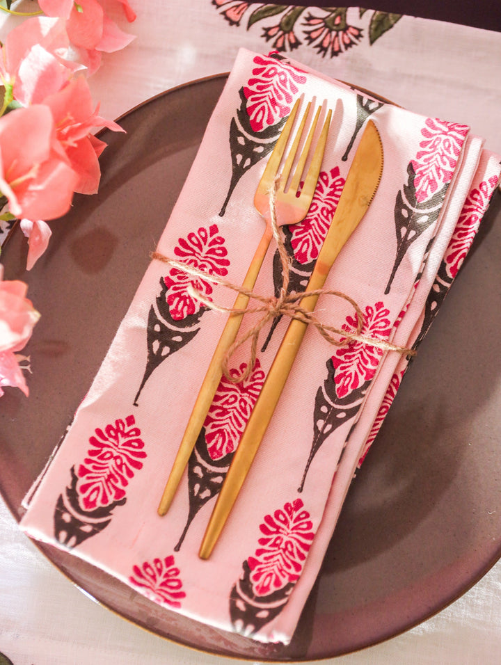 Pink napkin with black-and-red floral print on plate with gold cutlery