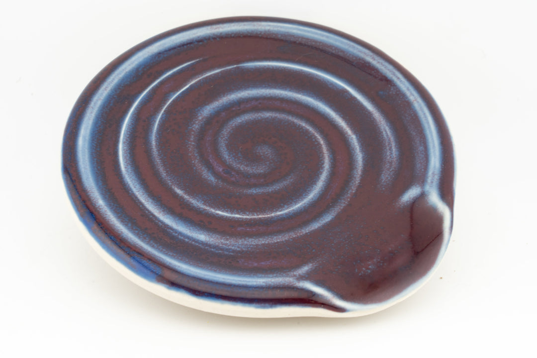 Brown ceramic spoon rest with concentric swirl grooves and raised rim