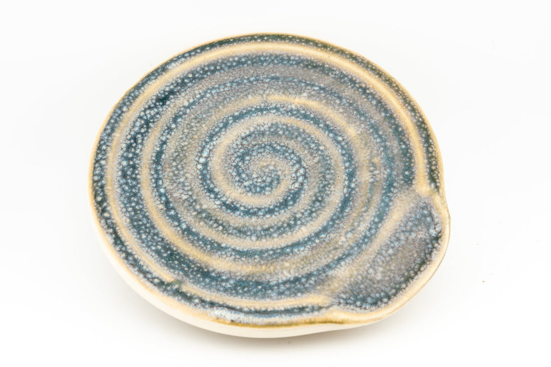 Blue speckled ceramic spoon rest with concentric swirl pattern and raised edge