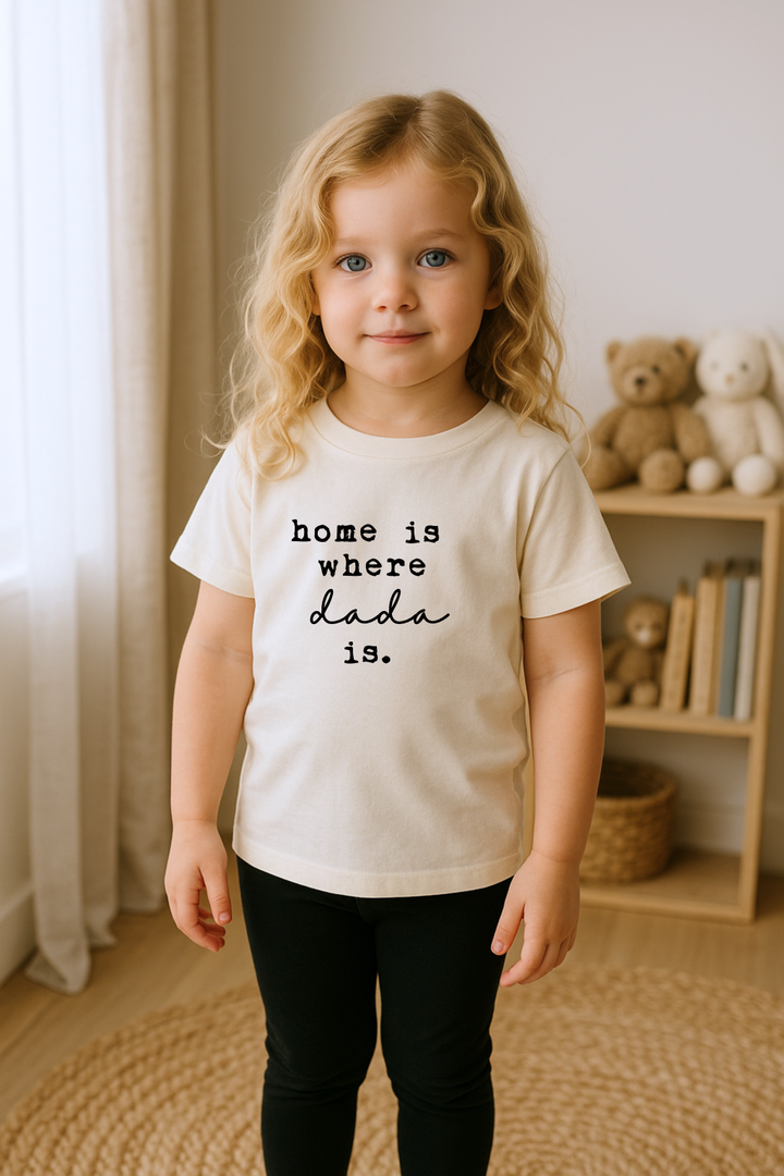 Kids organic T-shirt in cream on standing child, 'home is where dada is' front print.