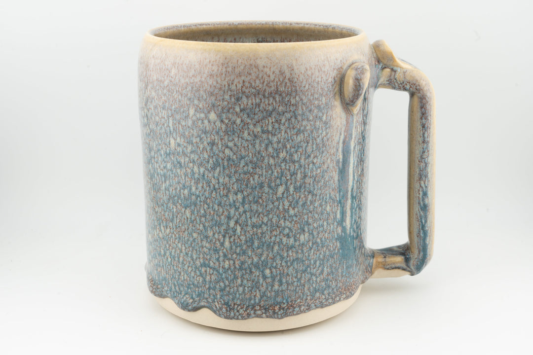 Blue ceramic stein mug with speckled glaze, rounded handle, caramel-brown rim