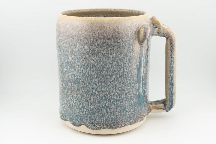 Blue ceramic stein mug with speckled glaze, rounded handle, caramel-brown rim