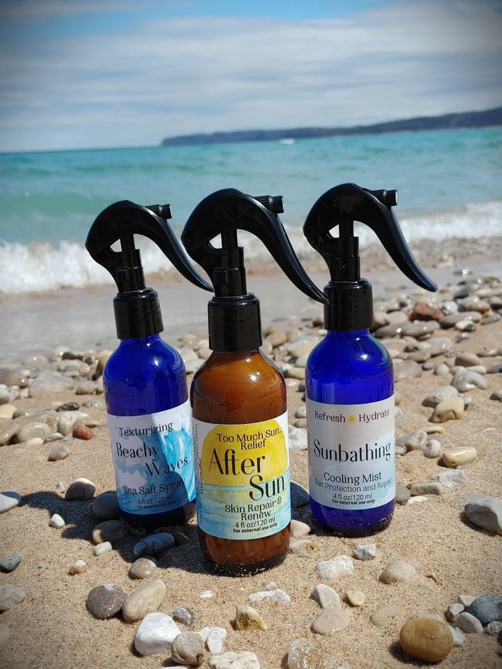 Three hair mist bottles with black spray triggers on beach sand