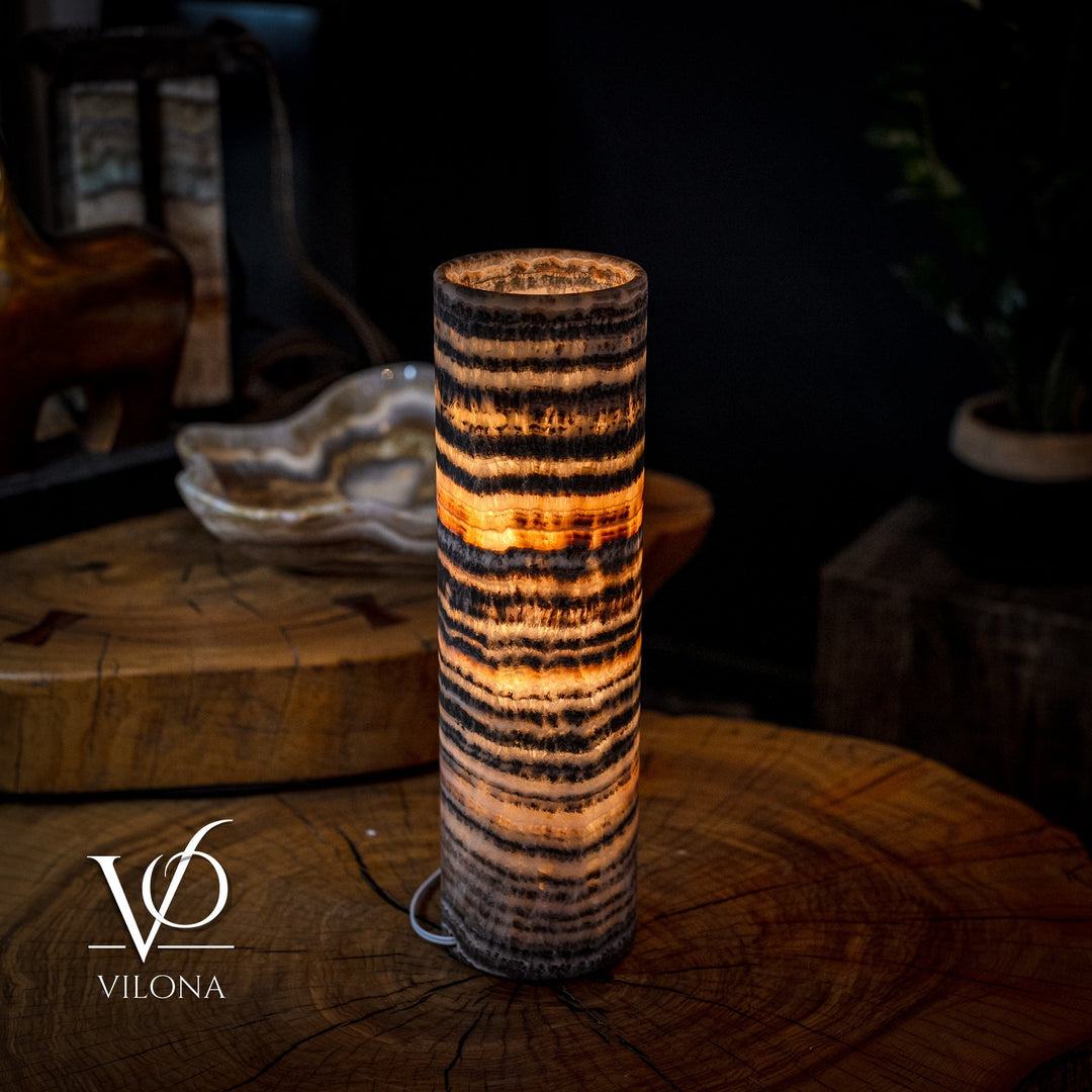 Tall cylindrical table lamp featuring amber-lit top and black-and-gold banded design