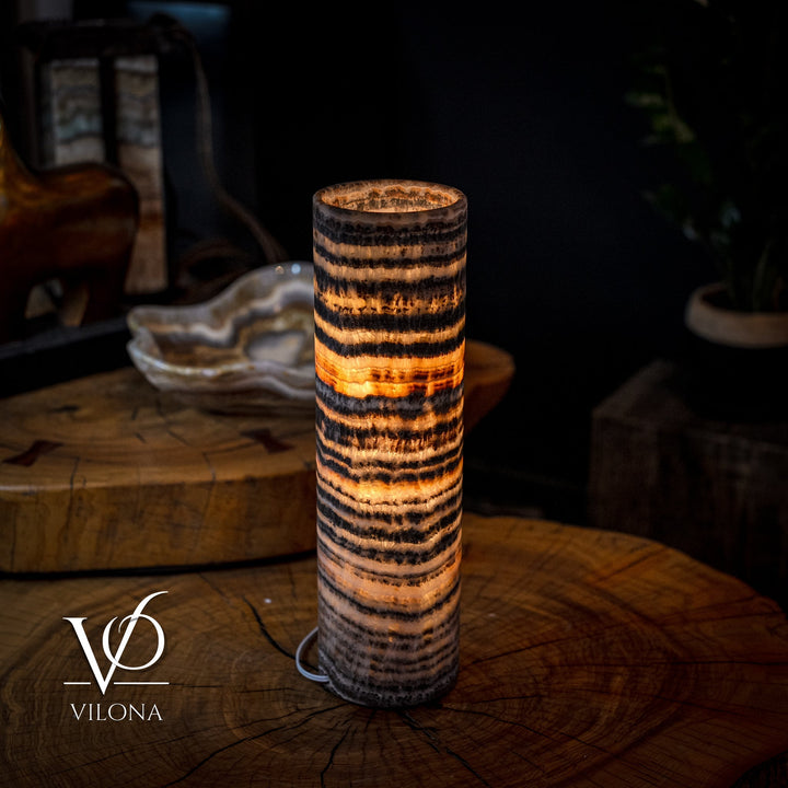 Tall cylindrical table lamp featuring amber-lit top and black-and-gold banded design
