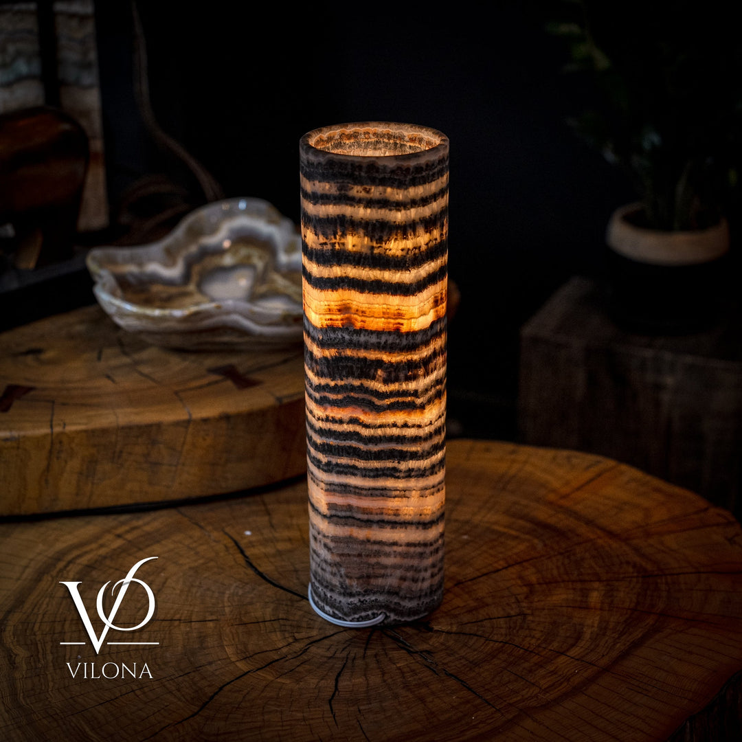 Cylindrical table lamp with warm orange interior glow and dark striped ceramic-stone body