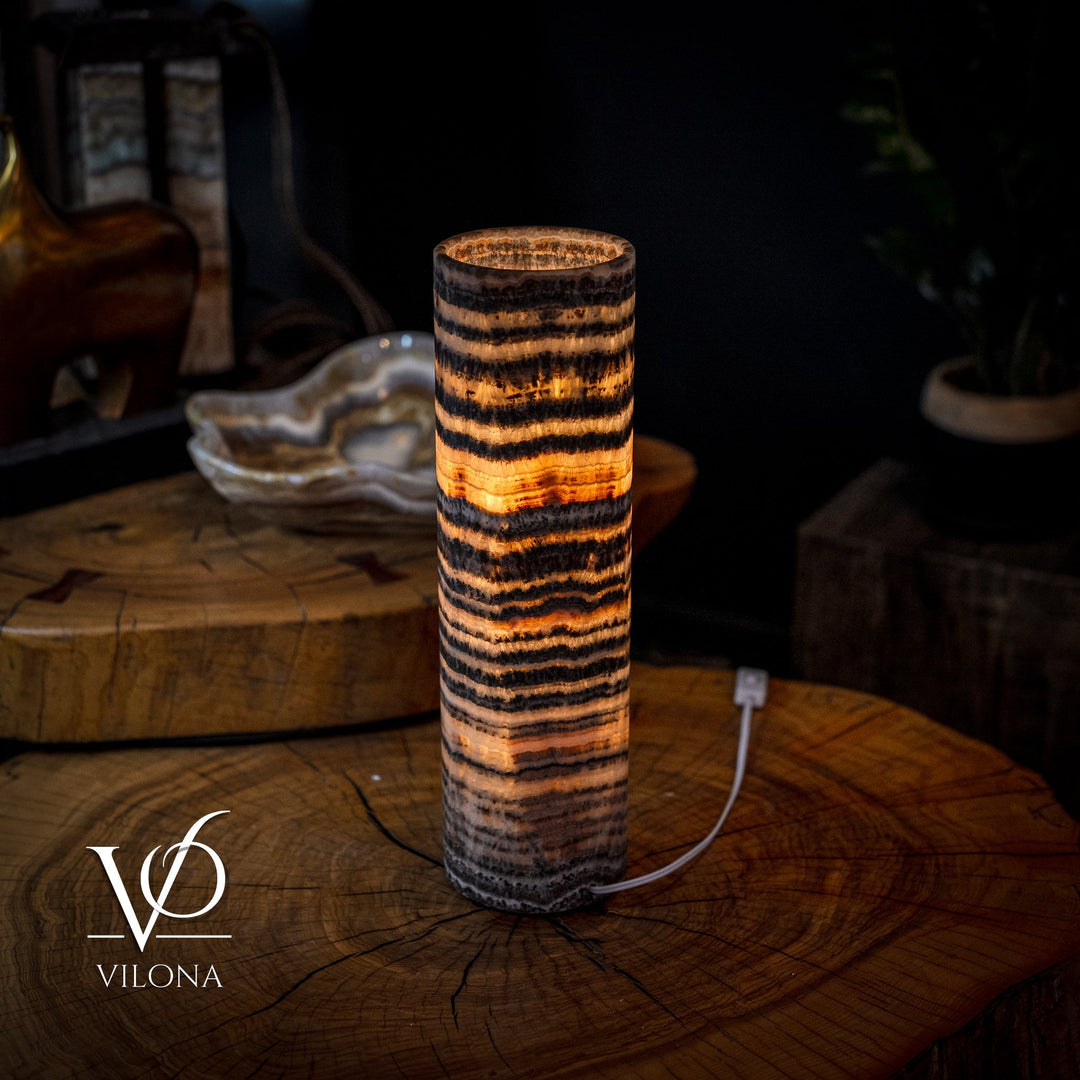 Cylindrical onyx table lamp with amber glow and black-and-gold striped surface