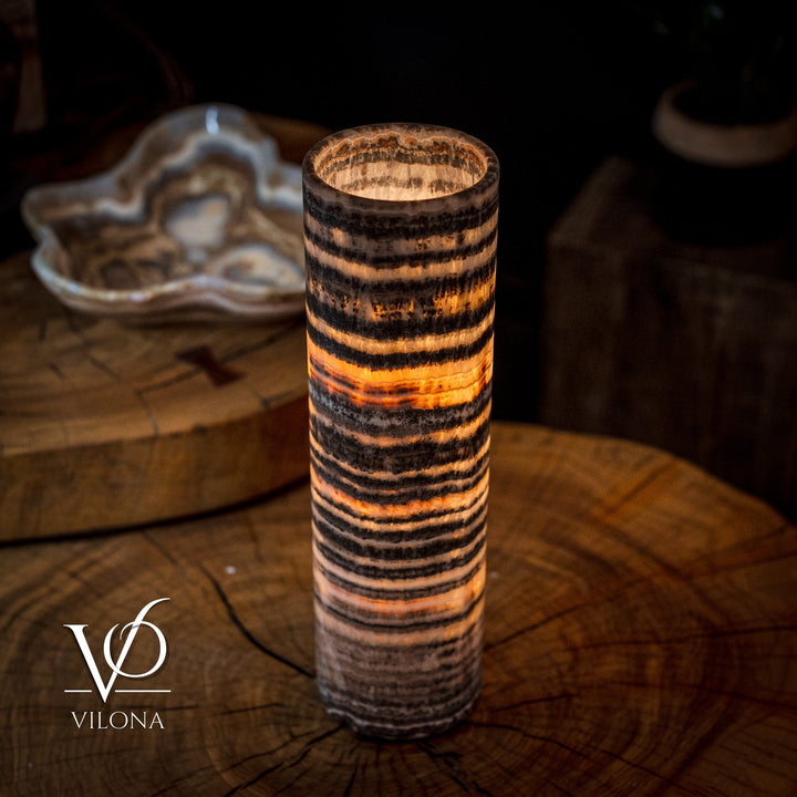 Cylindrical table lamp with glowing amber center and dark wavy striped texture