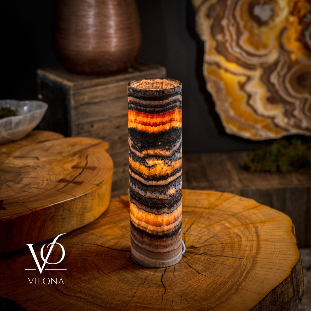 Cylindrical onyx crystal table lamp on wooden surface, warm orange glow through stripes.