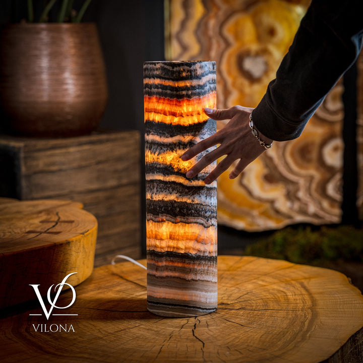 Cylindrical onyx crystal table lamp with warm orange glow; hand reaching toward it.