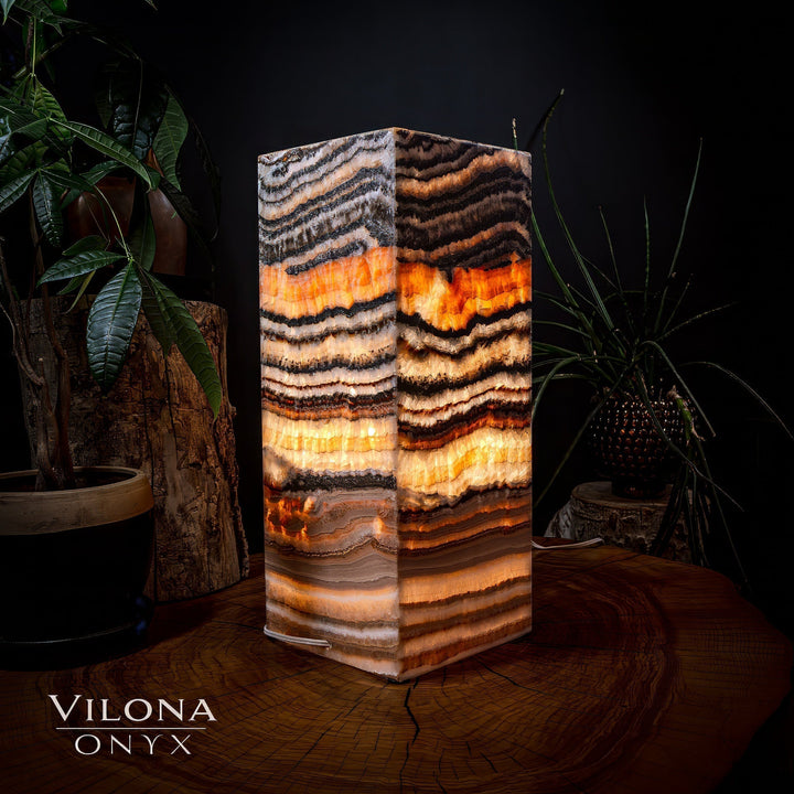 Medium square table lamp, close front view of striped onyx with warm orange illumination