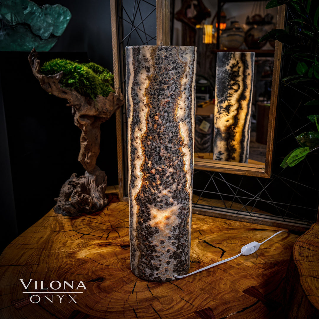 Onyx table lamp with tall cylindrical stone body, striped marbling, warm glow, power cord visible