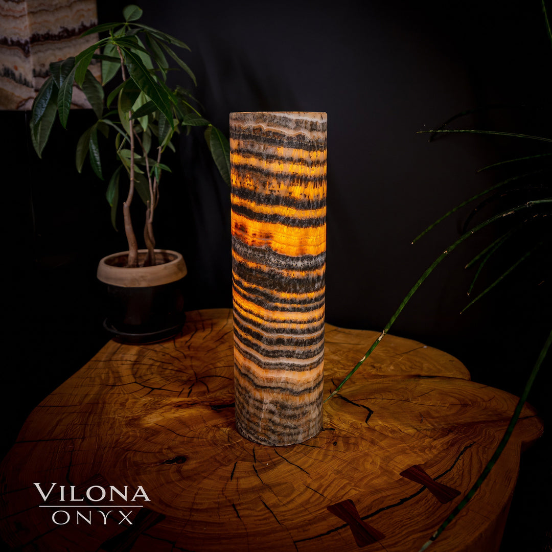 Tall cylindrical onyx table lamp with warm amber glow and dark horizontal striping.