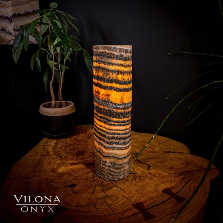 Tall cylindrical onyx table lamp with warm amber glow and dark horizontal striping.