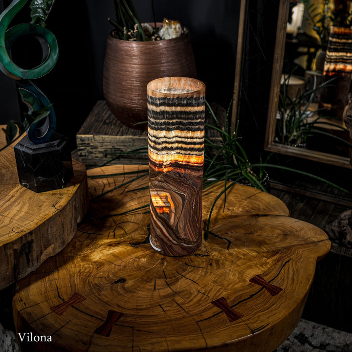 Cylindrical table lamp with stacked black stripes, cream bands, and warm lit glow