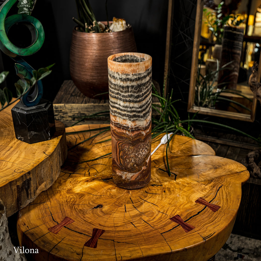 Cylindrical table lamp on wood surface with black wavy bands and warm amber light