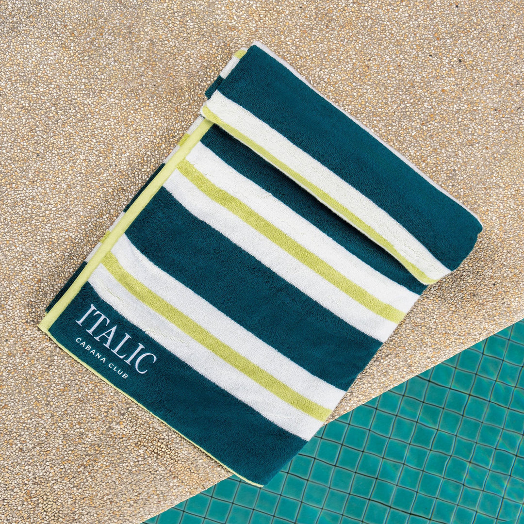 Cotton beach towel in teal and white with light green striped bands and “ITALIC” label.