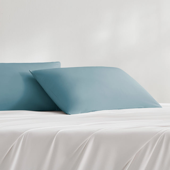 Teal-blue pillowcases on bed, two matching covers with envelope-style edges