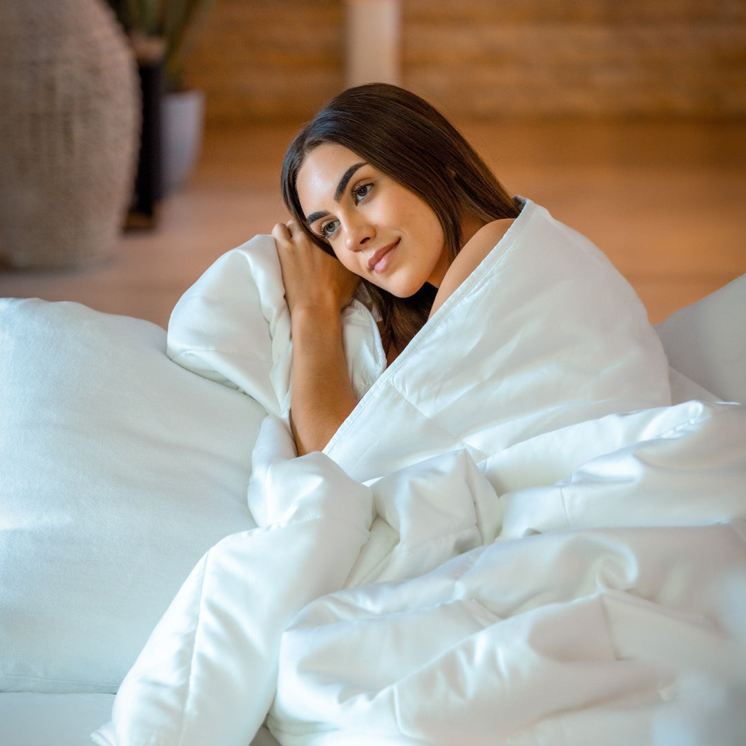 Light blue comforter draped on a bed, woman relaxing under the cover