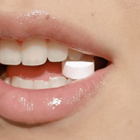 Close-up of teeth and gums with fluoride-free cinnamon toothpaste tablets dissolving