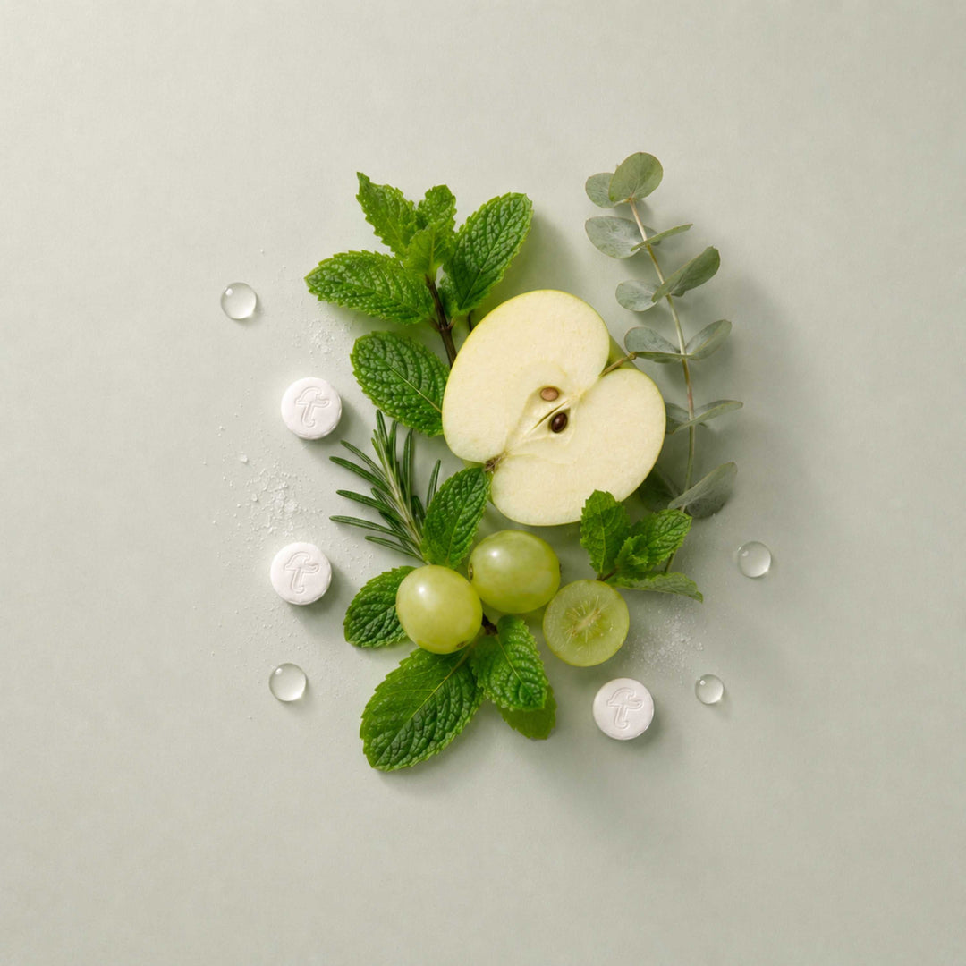 Toothpaste tablets with mint leaves, apple slices, and grapes on a clean surface