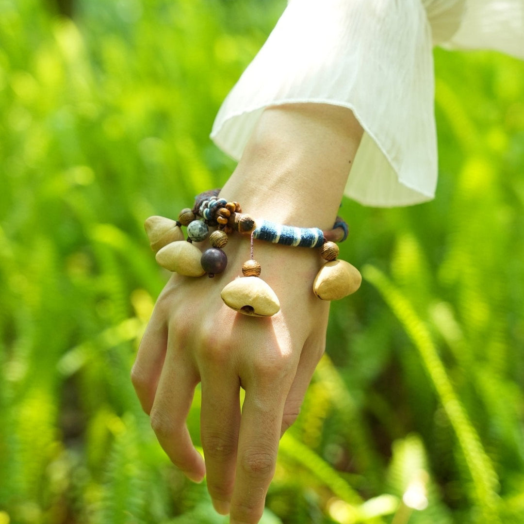 Seed bangle bracelet on wrist with tan pod charms and blue-and-white bead accents
