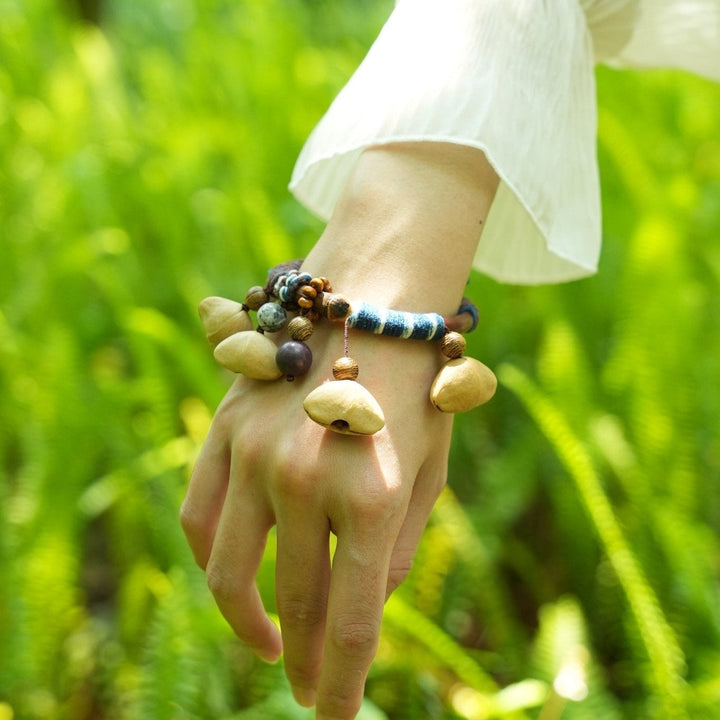 Seed bangle bracelet on wrist with tan pod charms and blue-and-white bead accents