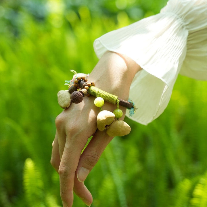 Braided seed bangle on wrist with brown beads and yellow-green hanging charms