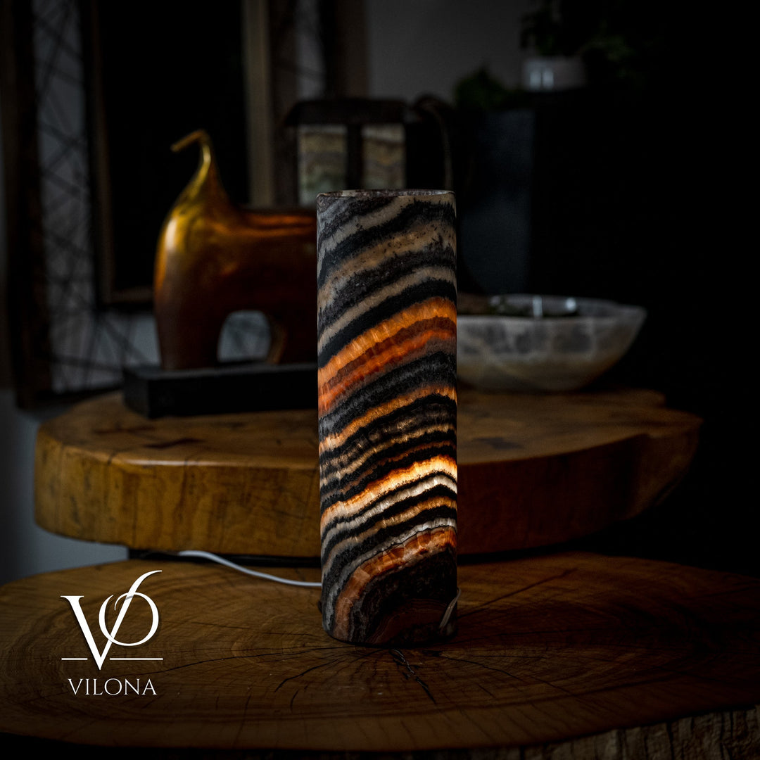 Full view of cylindrical onyx-look table lamp with black and orange striped shade