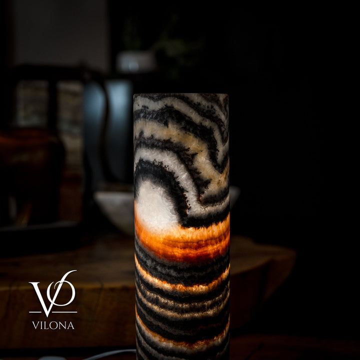 Cylindrical onyx-look table lamp shade with black stripe pattern and soft amber light