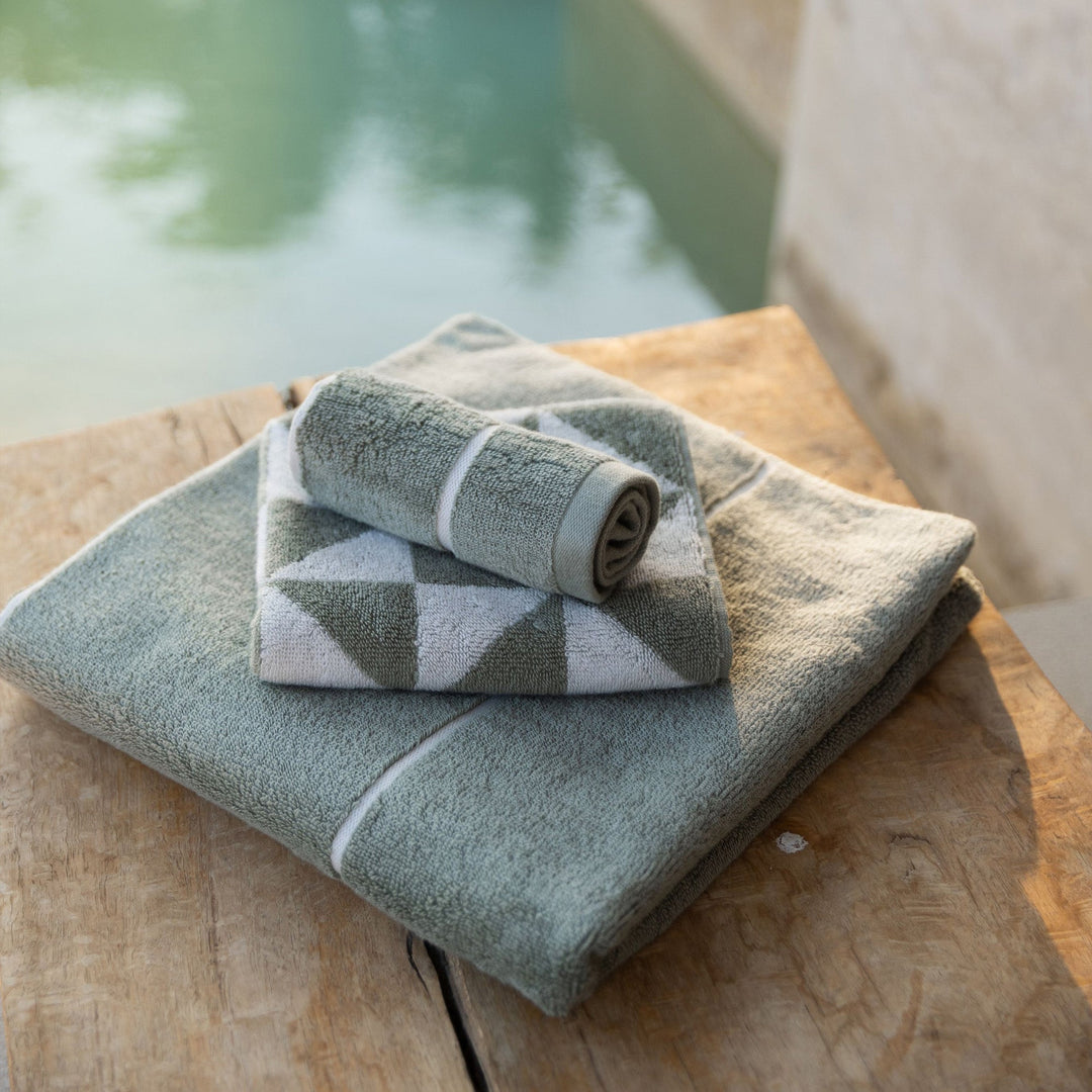 Rolled sage green and ecru cotton towels with geometric pattern