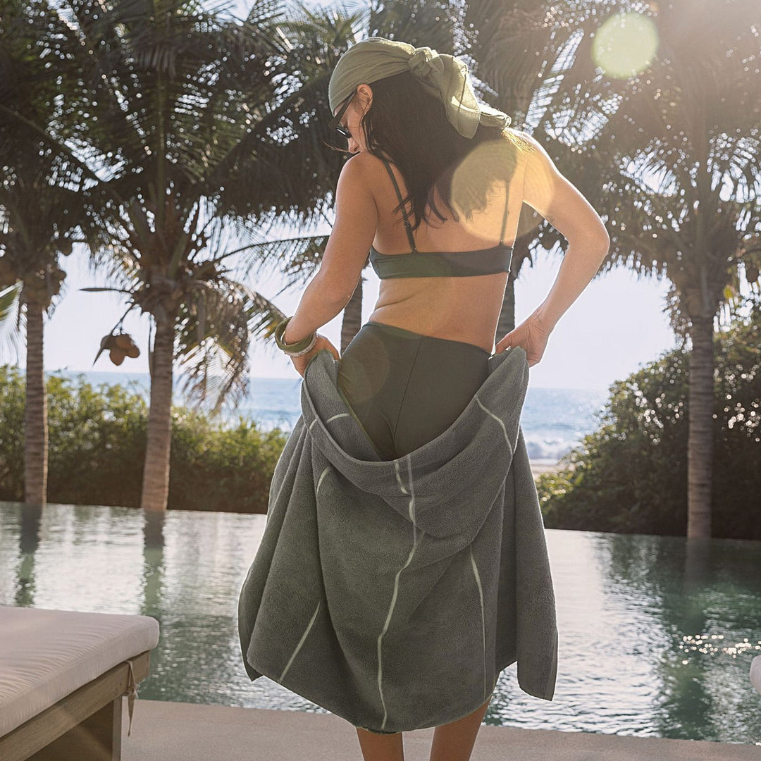 Sage-green hooded towel wrap worn over a swimsuit, draped at the back
