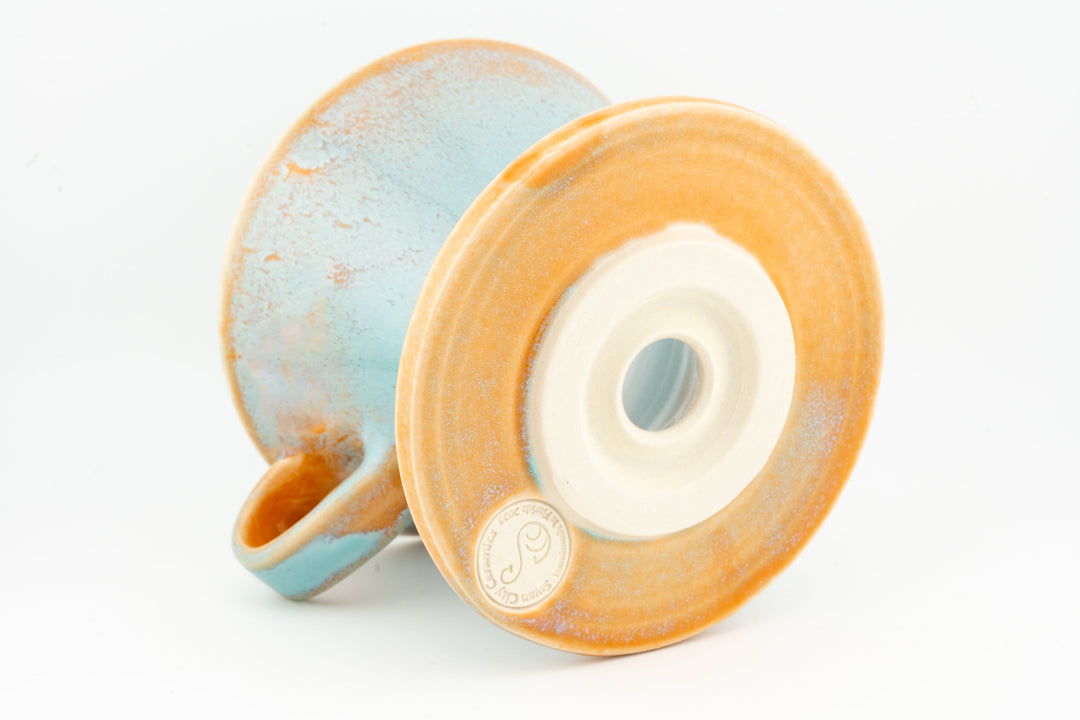 V60 ceramic coffee dripper underside with circular vent, speckled orange-and-blue glaze.