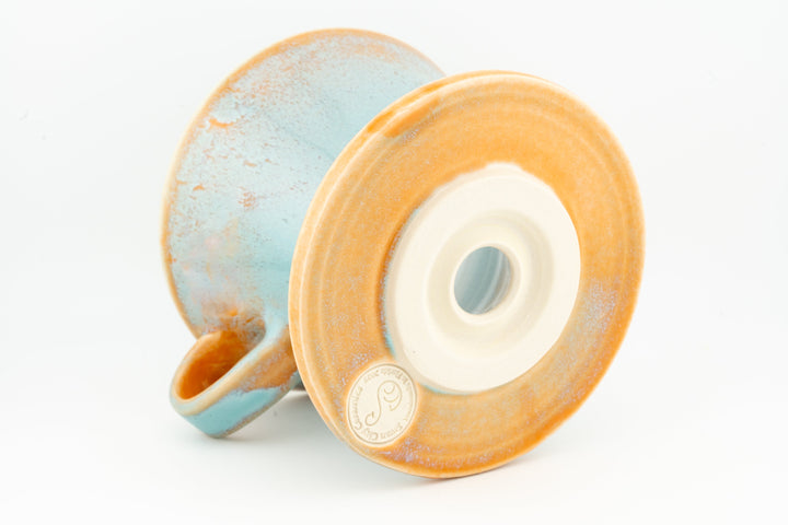 V60 ceramic coffee dripper underside with circular vent, speckled orange-and-blue glaze.