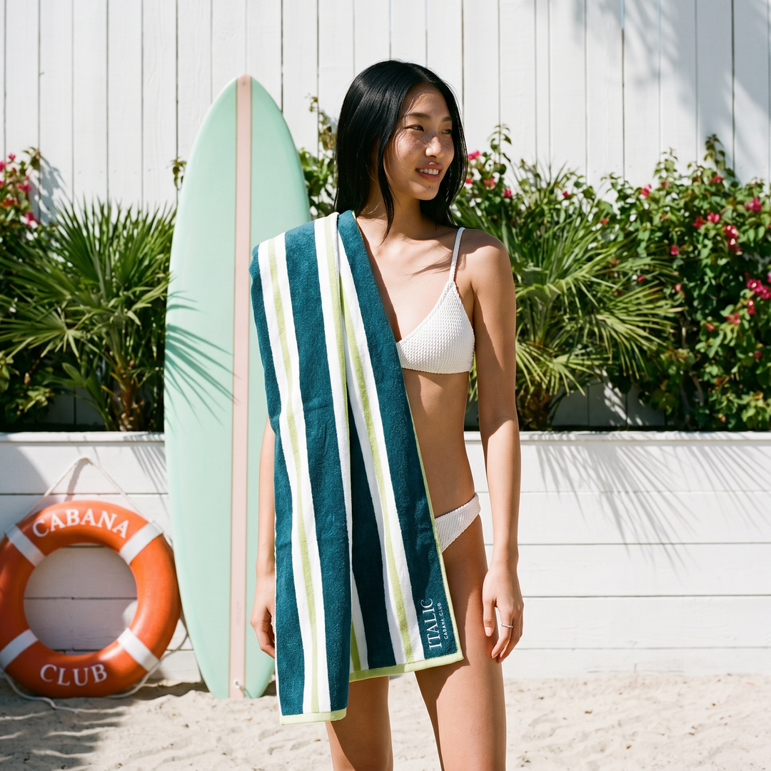 Cotton beach towel with teal and white vertical stripes hanging over a person’s hip.