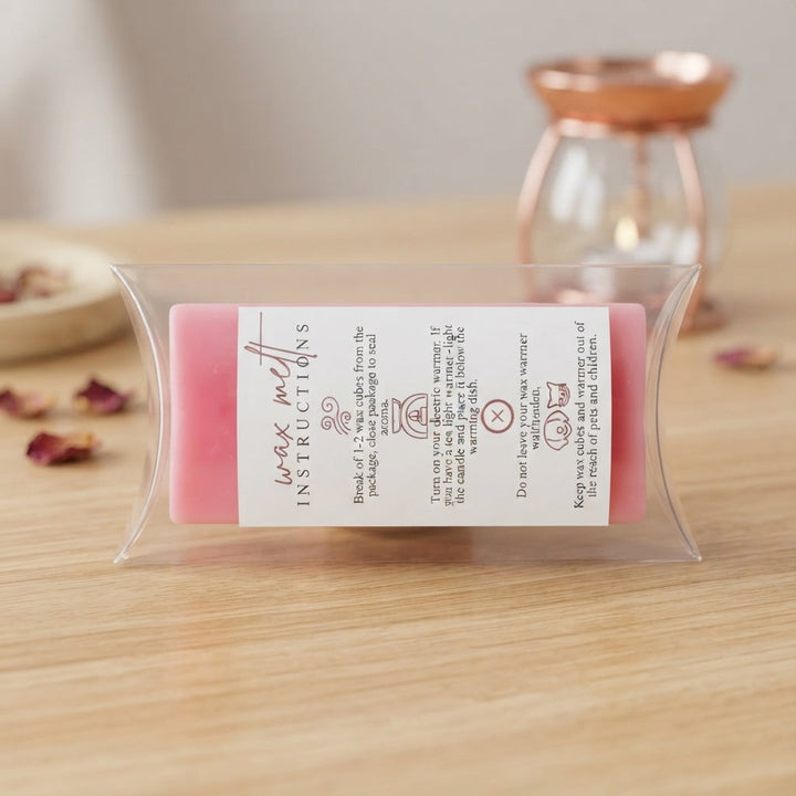 Clear plastic-wrapped wax melt bar with pink label and small ingredient text